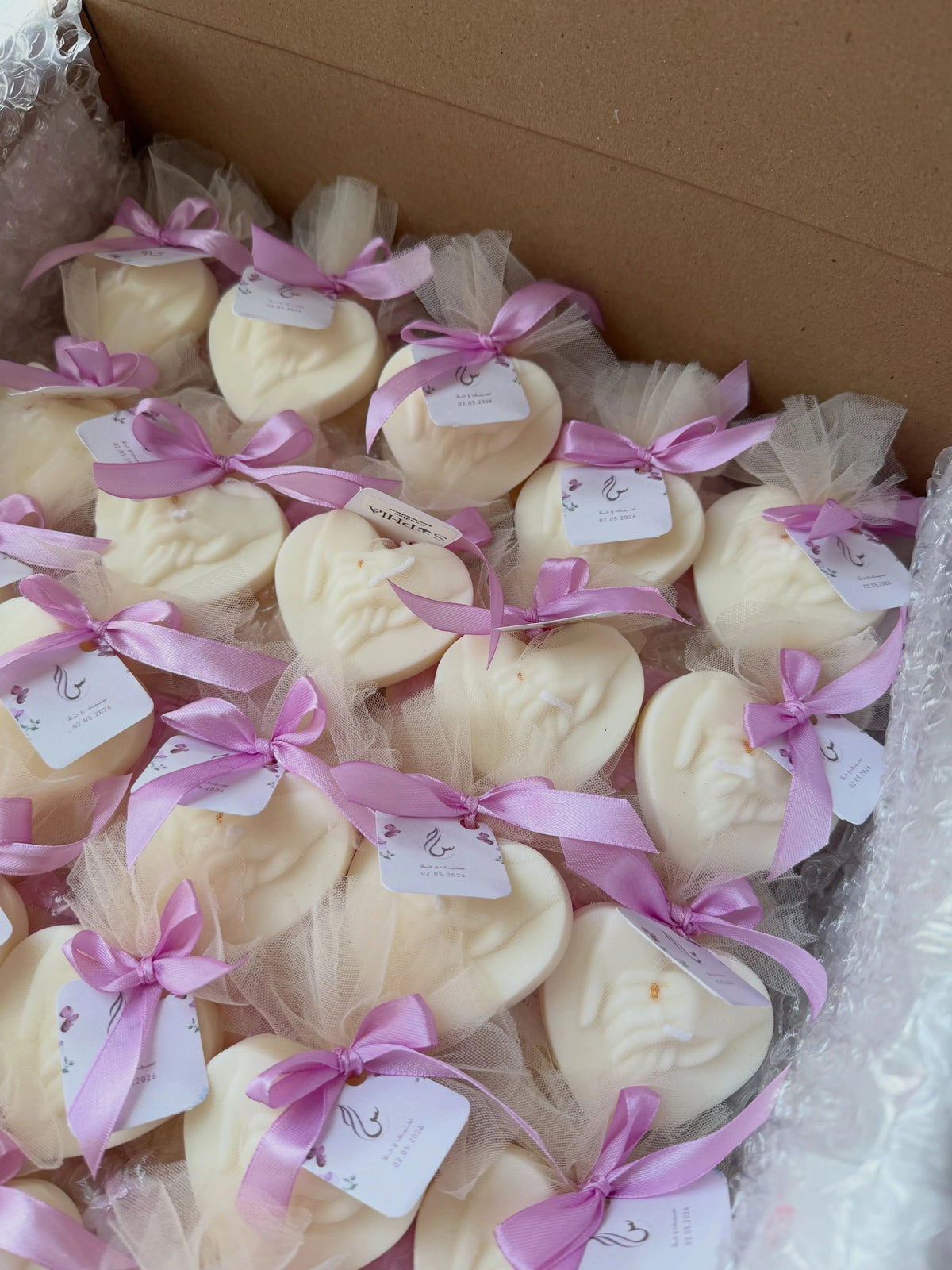 Ivory hands-in-heart candle favors wrapped in tulle with pink ribbons and personalized tags