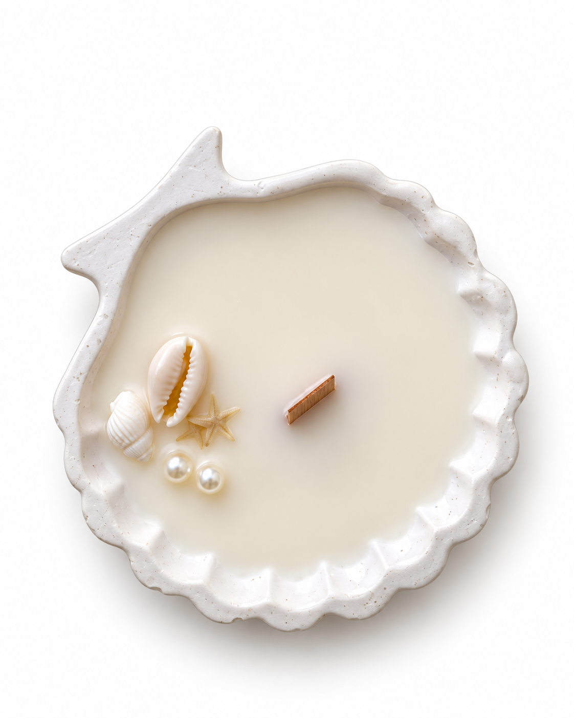 Small round ivory scalloped shell candle with wood wick, shells, and pearls on a white background